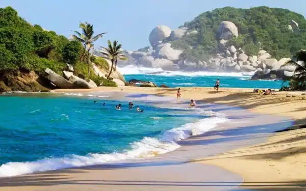 Playa de santa marta con personas nadando y rocas grandes